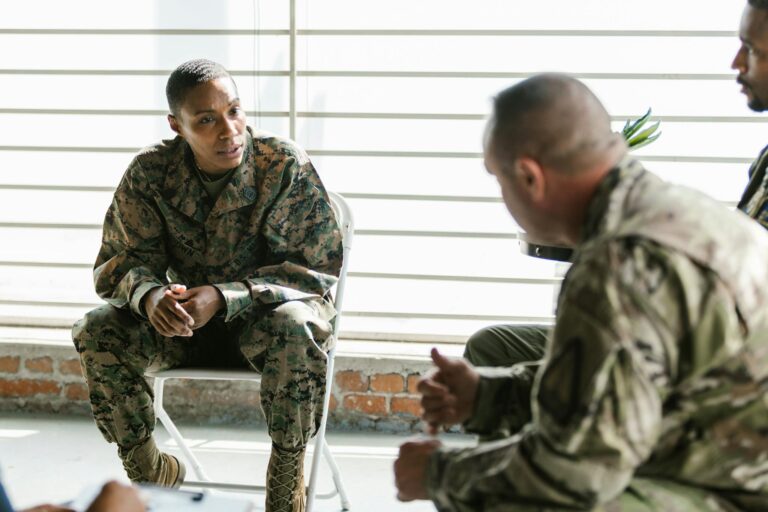Military veterans engage in a supportive group therapy session indoors.